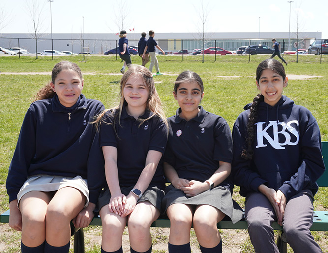 Four KBS students sitting together on a bench outside the school