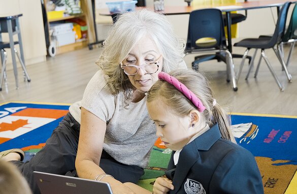 Teacher sitting beside a young student, helping with her work